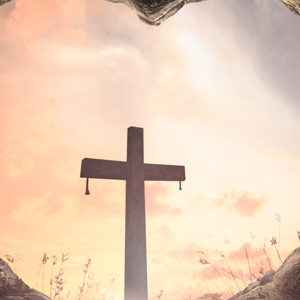 A large cross seen through a heart-shaped cave opening is silhouetted and bathed in light
