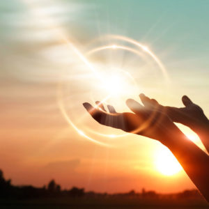 Lens flare is exaggerated to highlight backlit hands, raised to the sky in prayer