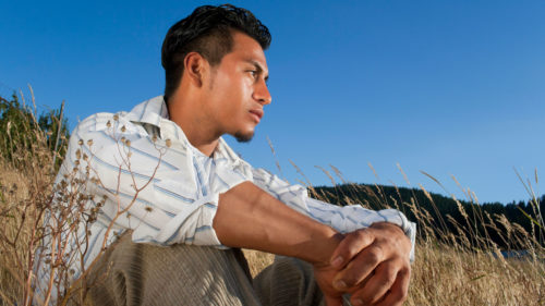 A pensive hispanic man sits with his arms crossed over his knees