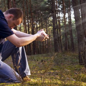 A man prays furvently in a mossy, wooded area outside