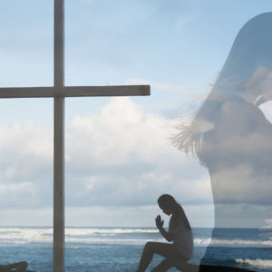 Woman kneels beside a cross on the shoreline