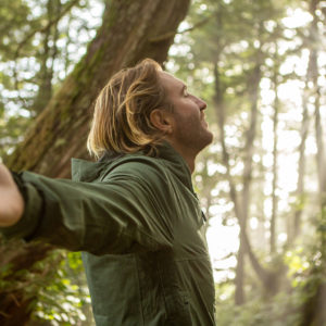 Profile of a man with eyes closed and arms outstreched, in a peaceful forested setting