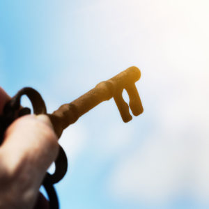 Figurative image of a key being held up to a glowing light against blue sky