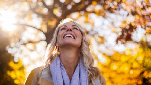 A joyful woman backlit by autumn foliage and sunlight