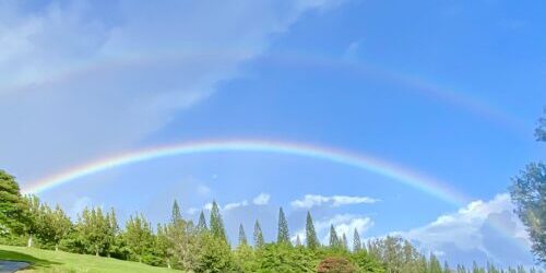A double-rainbow glows against a bluebird sky