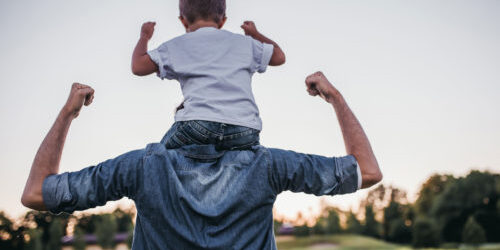 A boy sits on his father's back, both raising their fists in celebration