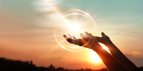 Lens flare is exaggerated to highlight backlit hands, raised to the sky in prayer