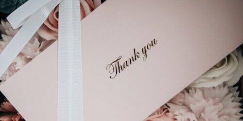Thank You is printed on an envelope in cursive, on a background of light-pink and white flowers and white ribbon (Insung Yoon, UnSplash)