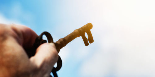 Figurative image of a key being held up to a glowing light against blue sky