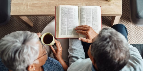 An older couple read from a bible and sip coffee