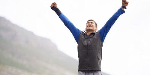 A man wearing a windbreaker raises his arms victoriously, with his eyes shut tightly